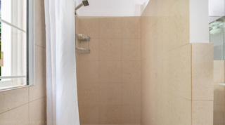 Walk-in curtained shower with a garden window at Jamoon villa, Barbados