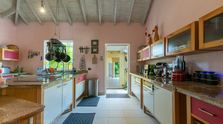 Kitchen with pink walls, hanging pot rack and granite worktops at Jamoon villa in Barbados
