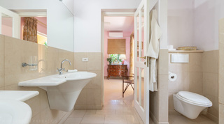 Bathroom with wall basin and WC opening to a pink bedroom at Jamoon, Barbados