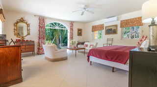 Spacious bedroom with king bed, red throw and a seating area at Jamoon, Barbados