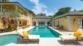 Sunlit pool and yellow two-storey facade with twin sun loungers at Jamoon, luxury villa in Sandy Lane, Barbados