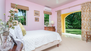 Pink bedroom with arched doors to the garden and an antique chest at Jamoon villa in Barbados