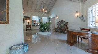 Coral-stone entrance hall with antique desk and palm planter at Jamoon, Sandy Lane Estate, Barbados