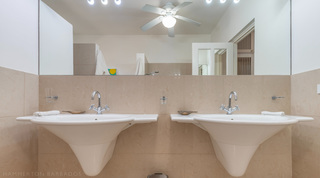 Bathroom with twin wall basins, large mirror and ceiling fan at Jamoon villa in Barbados