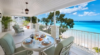 Kiko Villa balcony seating and glass table set for breakfast with views across the sea and blue skies through tree branches