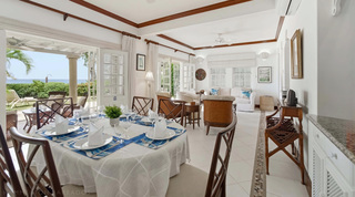 Indoor dining table with blue linens beside open doors to the sea terrace, Fathom's End villa, Barbados