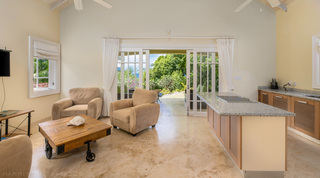 Cottage living area with taupe armchairs, a wheeled cart table and granite kitchen island, Monkey Hill in Barbados