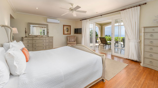 Cream upholstered bed and glazed doors onto a sea-view terrace at Monkey Hill, St. James luxury villa, Barbados
