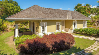 The separate cottage at Monkey Hill in Barbados, with a covered porch, green-cushioned sofas and a stepping-stone path