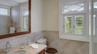 White louvred shutters and a diamond-pattern transom window in a tiled Monkey Hill en-suite, Barbados