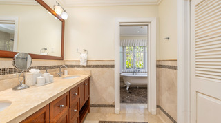 Double-basin wooden vanity with a doorway framing a clawfoot bath in an en-suite bathroom at Monkey Hill in Barbados