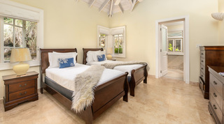 Twin dark-wood sleigh beds with faux-fur throws beneath a beamed vaulted ceiling, Monkey Hill holiday villa, Barbados