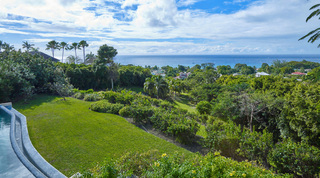 Sloping lawns and gardens below the curved pool edge, with sea views beyond, at Monkey Hill in Sugar Hill, Barbados