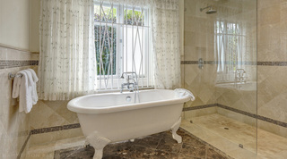 Clawfoot roll-top bath before a curtained garden window, beside a walk-in rain shower, Monkey Hill villa in Barbados