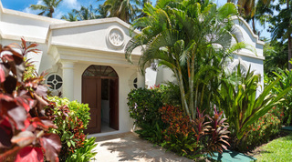 Twin palm emblem above the arched doorway of Mullins Bay Villa – Twin Palms in Barbados, framed by tropical shrubs