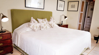 Bedroom with king bed, green headboard and campaign chests beneath framed prints at Mullins Mill, Barbados