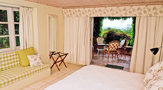Bedroom with a gingham window seat and doors opening to a sea-view terrace at Mullins Mill villa, Barbados