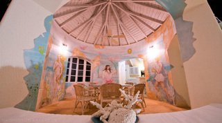 Round dining room beneath a timber cone ceiling with painted sea murals and a coral centrepiece at Mullins Mill, Barbados