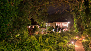 Villa lit at night above lush ferns and an uplit garden path at Mullins Mill, St. Peter, Barbados