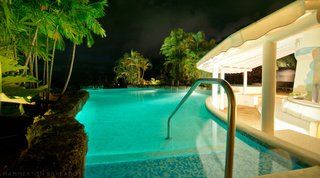 Ridge-side infinity pool lit at night beside the beach house pavilion at Mullins Mill, private villas in Barbados