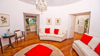 Circular sitting room with chandelier and red and cream sofas on a polished wood floor at Mullins Mill, Barbados