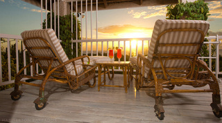 Two cane sun loungers and cocktails on a timber deck at sunset over the coastline at Mullins Mill, Barbados