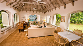 Cottage sitting room under a timber-beamed ceiling with arched windows and cane chairs at Mullins Mill, Barbados