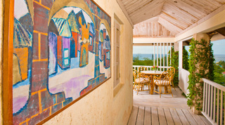 Covered verandah with a framed townscape painting and cane dining set overlooking the sea at Mullins Mill, Barbados