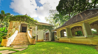 Weathered stone cottage with external stair beside an arched verandah at Mullins Mill, private villas in Barbados