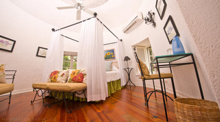 Round bedroom with an iron four-poster bed and white drapes on a wood floor at Mullins Mill, Barbados