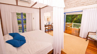 Four-poster bedroom with blue cushions and doors to a garden-view balcony at Mullins Mill, luxury villa in Barbados