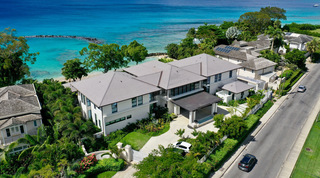 Coast-road aerial of One Beachlands villa and its gardens, turquoise sea beyond, Barbados