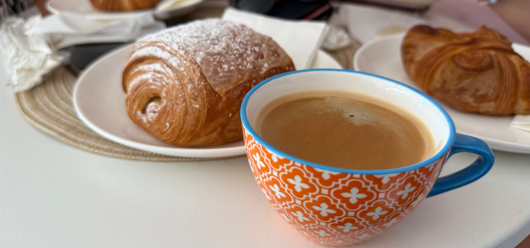 A flaky, icing-sugar-dusted pain au chocolat and a coffee in a patterned cup at The Cliff Bakery