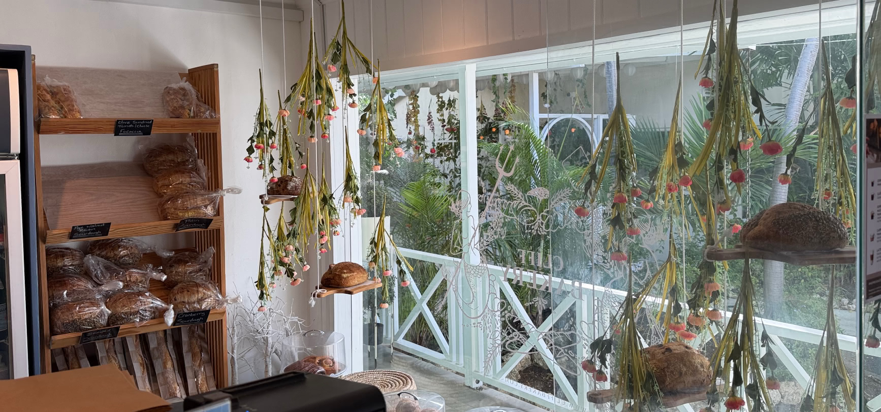 Inside The Cliff Bakery: hanging dried flowers, shelves of artisan sourdough and the mermaid window beyond