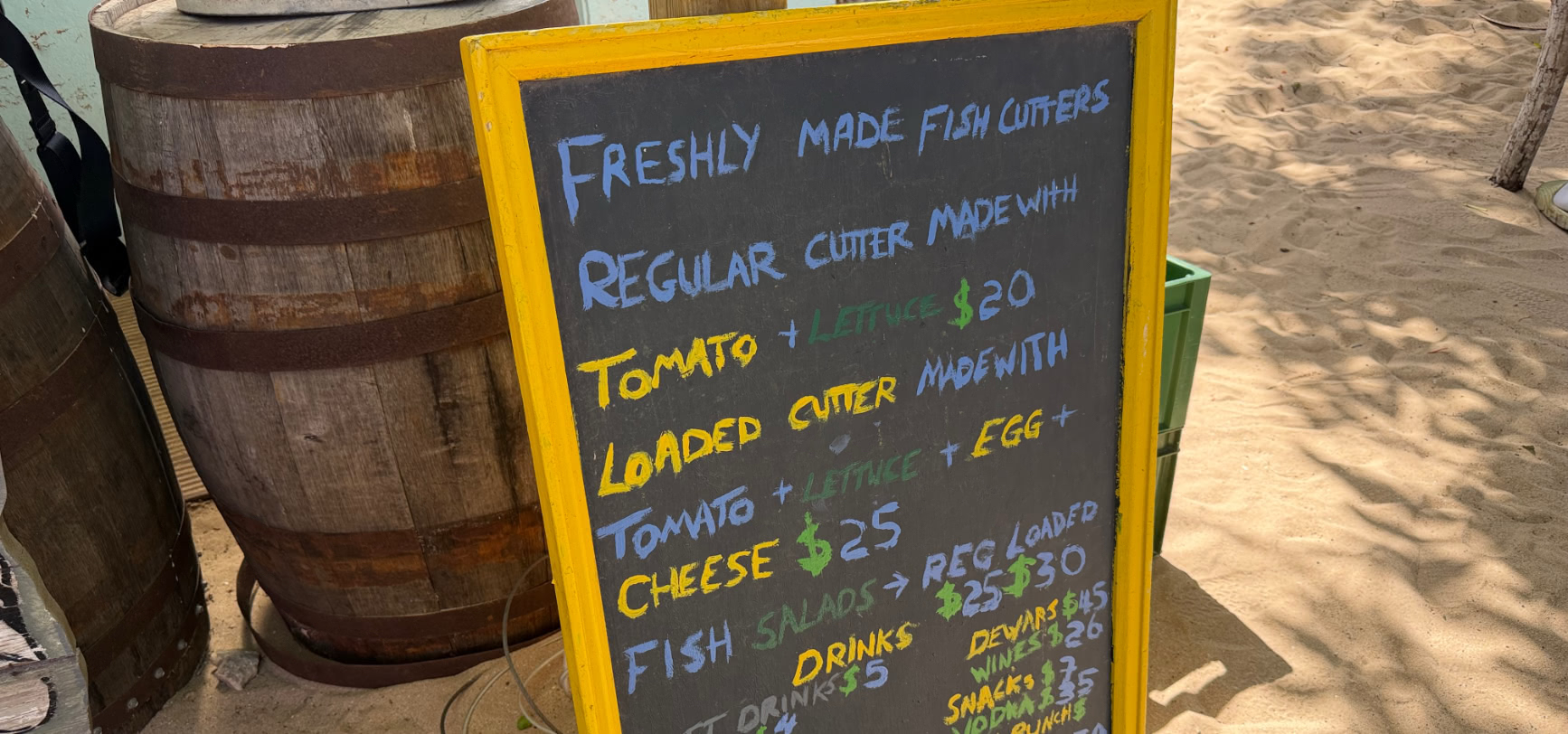 The yellow-framed chalkboard menu at Caboose listing freshly made fish cutters — regular cutter $20, loaded cutter $25, fish salads $25 and $30 — and drinks
