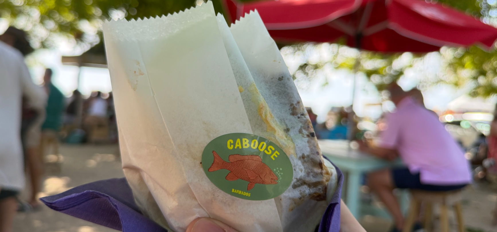 A Caboose fish cutter wrapped in greaseproof paper sealed with the round green CABOOSE Barbados fish sticker