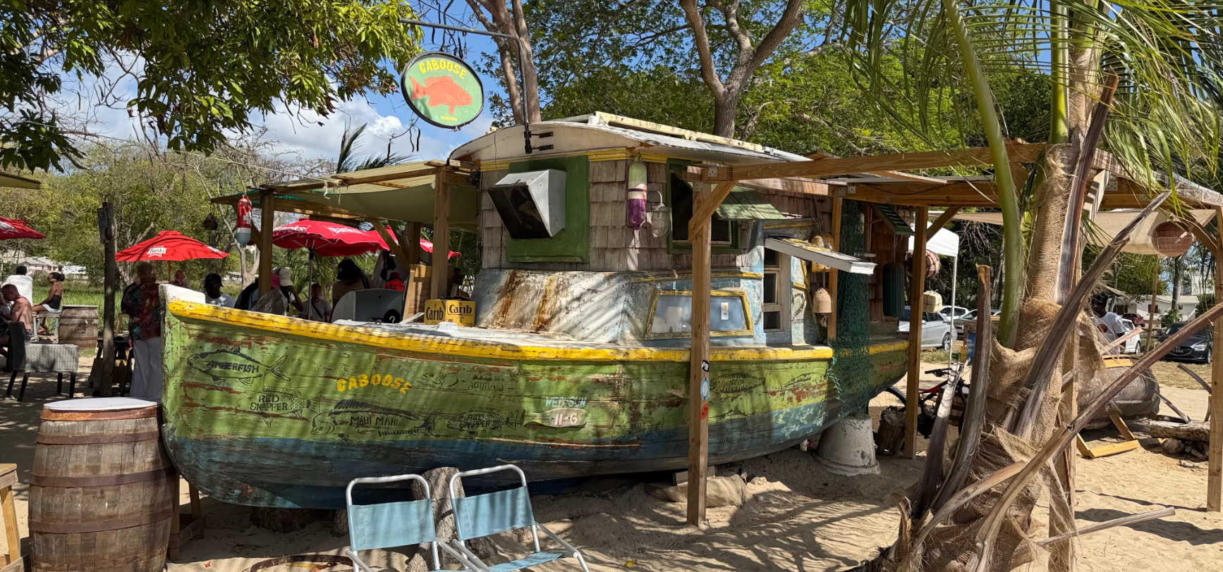 The hand-painted fishing boat at Caboose Barbados, beached on the sand at the north end of Speightstown, beneath the oval CABOOSE fish sign