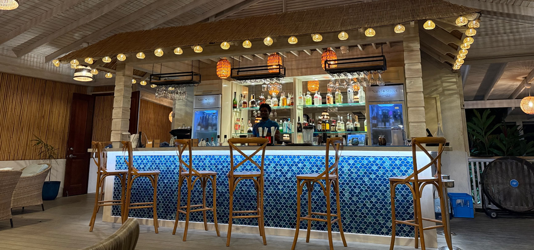 The driftwood bar with its blue mosaic-tile front, rattan stools and string lights