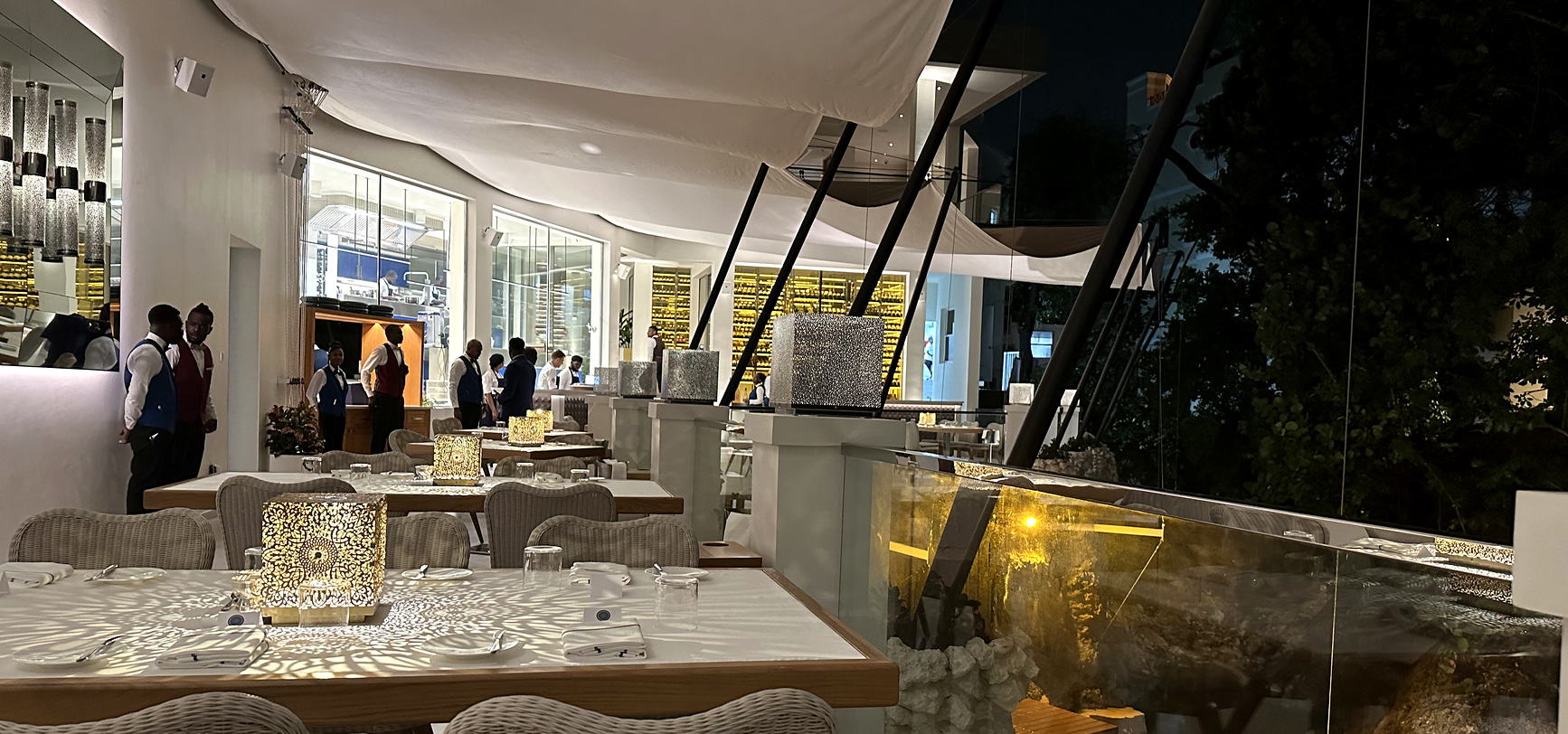 The dining room at The Cliff after dark, pierced lanterns throwing lacework light across the white tables
