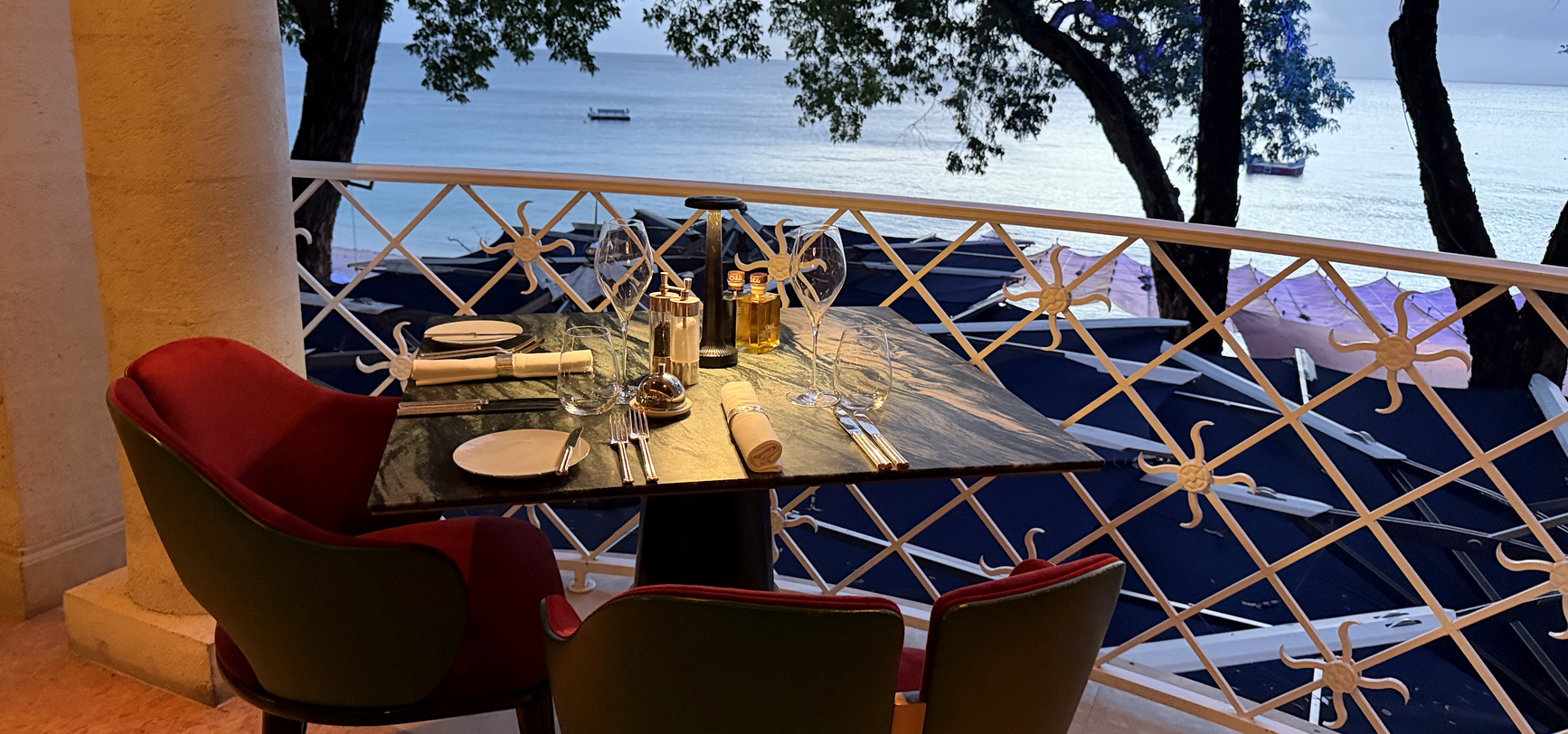 A table for two on the terrace at The Monkey Club at dusk, red and green velvet chairs above the Sandy Lane beach