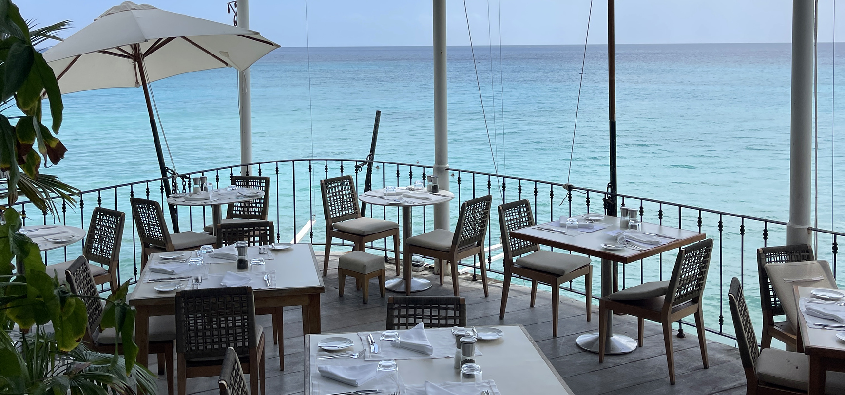 Laid tables on the terrace at Cliff Beach House, the deck curving out above turquoise water