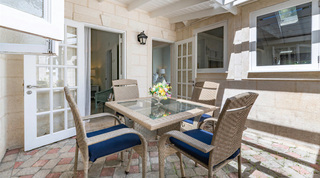 Courtyard with a wicker table for four on grey and terracotta pavers by glazed bedroom doors, Queens Fort Pavilion, Barbados
