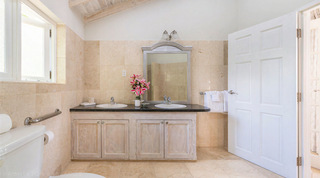 Whitewashed wood vanity with twin basins, an arched silver-toned mirror and pink lilies at Queens Fort Pavilion, Barbados