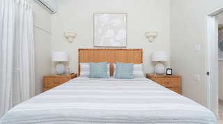 Queens Fort Pavilion bedroom with a woven cane headboard and turquoise cushions beneath textured white artwork, Barbados