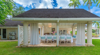 Curtained dining pavilion with a dark shingle roof beside the pool deck at Queens Fort Pavilion villa in Barbados