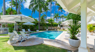 Pool, white sun loungers and a stone dolphin sculpture seen from the shade at Queens Fort Pavilion villa, Barbados