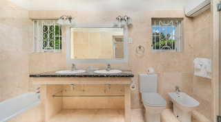 Bathroom with twin basins beneath a white-framed mirror between scroll-grilled windows at Queens Fort Pavilion, Barbados