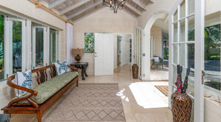 Queens Fort Pavilion entrance hall with a scrolled-metal chandelier, carved bench and doors open to the courtyard, Barbados