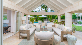 Covered terrace lounge with wood-framed sofas under a sunburst fretwork gable, Queens Fort Pavilion holiday villa in Barbados