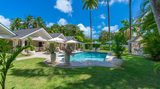 White sunburst gables, pool and pool bar beneath tall palms from the lawn at Queens Fort Pavilion near Holetown, Barbados